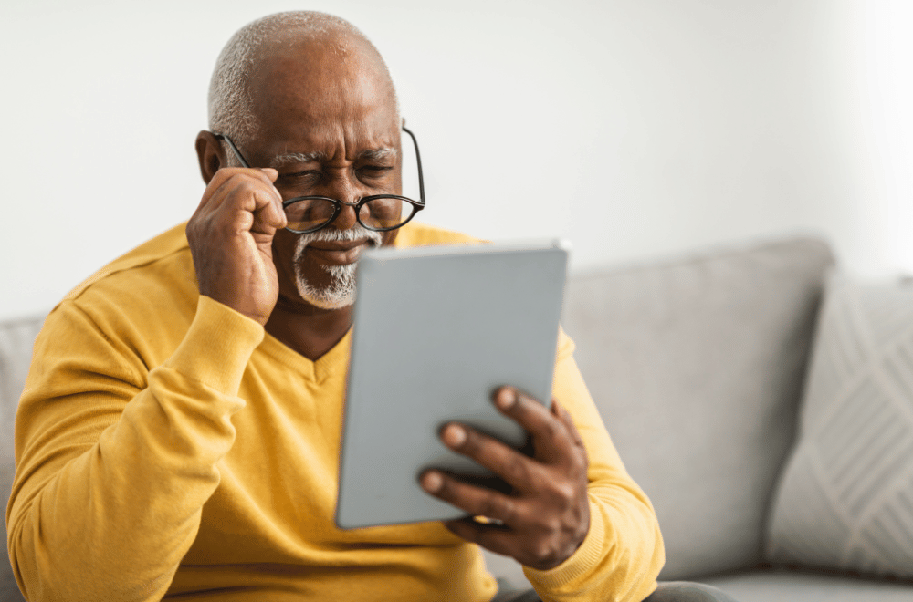 older man with glasses having trouble seeing a tablet in his hand